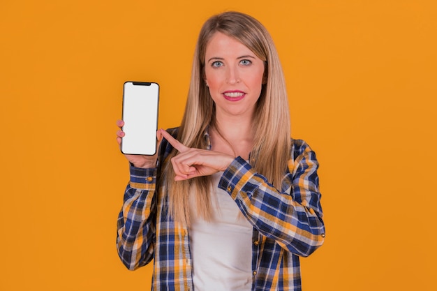 Smiling young businesswoman pointing his finger at mobile phone against an orange background