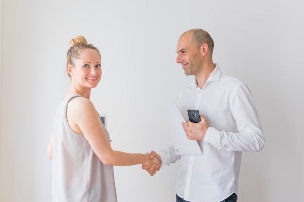 Free photo smiling young businesswoman shaking hand with businessman holding paper and cellphone