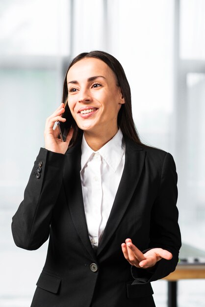 Smiling young businesswoman taking on cellphone shrugging