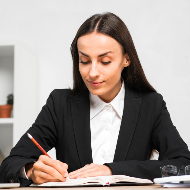 Smiling young businesswoman writing notes of diary with pencil