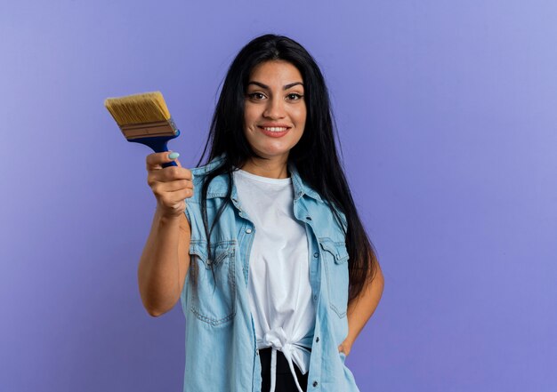 Smiling young caucasian girl holds paint brush isolated on purple background with copy space