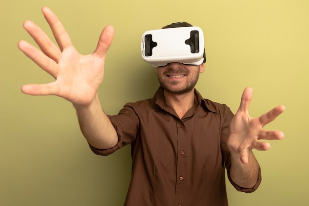 Smiling young caucasian man wearing vr headset spreading hands isolated on olive green background