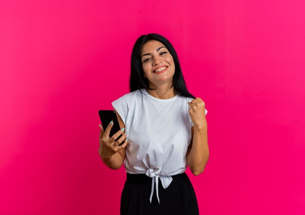 Smiling young caucasian woman holds phone and keeps fist