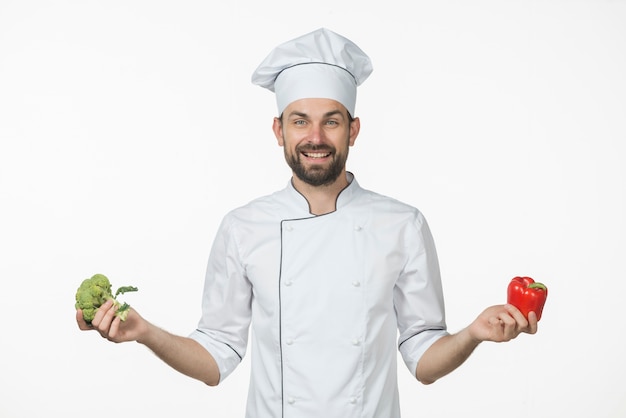 Smiling young chef holding fresh green broccoli and red bell pepper in his hand