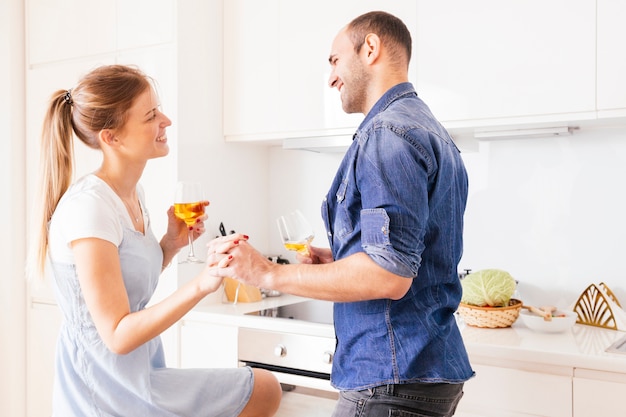 Smiling young couple holding each other's hand holding wineglasses in hand looking at each other