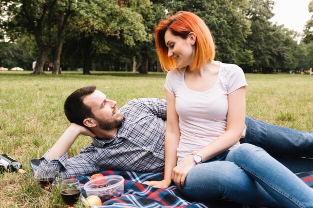 Smiling young couple lying on blanket over green grass with many fruits