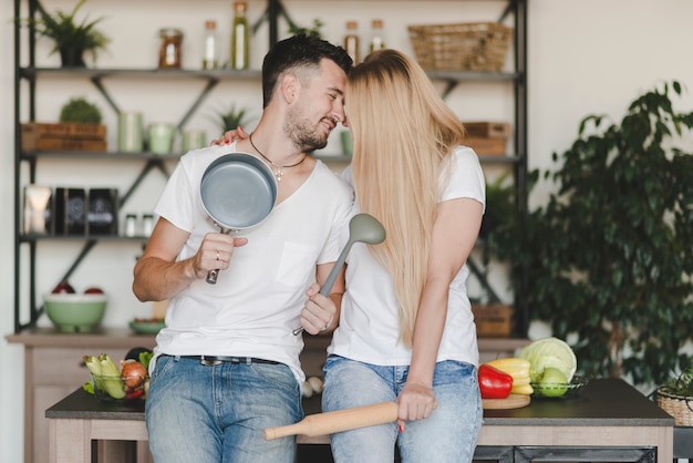 Free Photo smiling young couple sitting on kitchen counter holding utensil