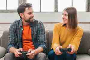 Free photo smiling young couple sitting on sofa looking at each other while playing video game