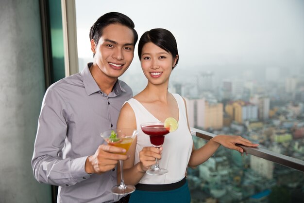 Smiling Young Couple with Cocktails on Balcony