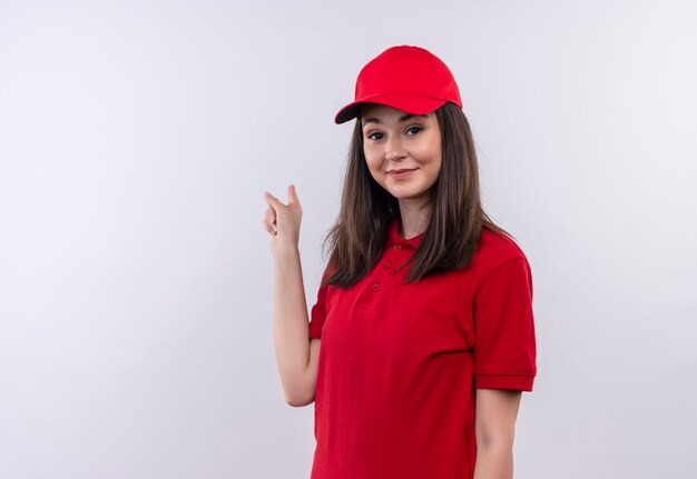 Smiling young delivery woman wearing red t-shirt in red cap points back on isolated white wall