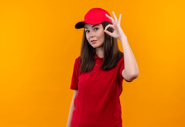 Free photo smiling young delivery woman wearing red t-shirt in red cap and shows okey gasture on isolated yellow wall