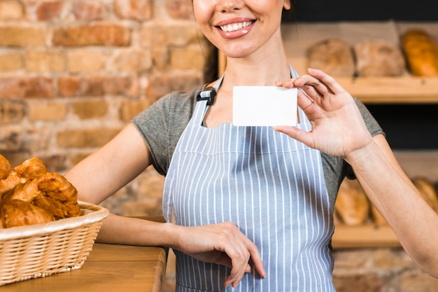 Free photo smiling young female baker showing white visiting card in the bakery shop