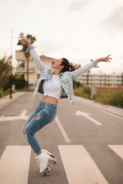 Smiling young female skater dancing with roller skate on road