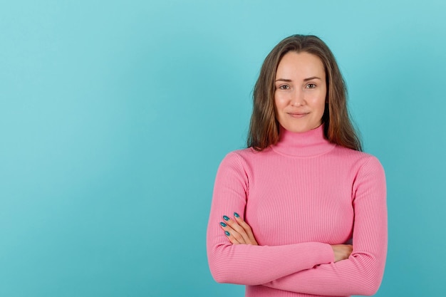 Smiling young girl is looking at camera by crossing arms on blue background