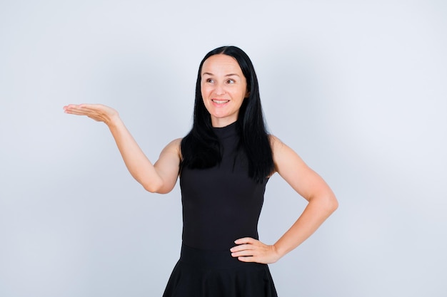 Smiling young girl is looking up and pointing left with hand on white background