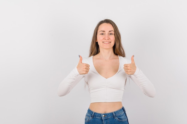 Smiling young girl is showing perfect gestures with thumbs on white background