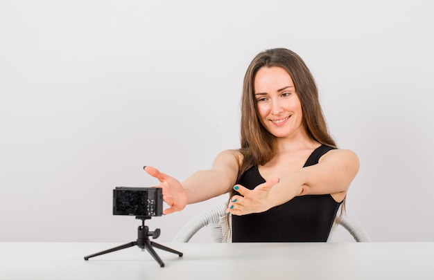 Smiling young girl is taking photo with camera by extenting hands on white background