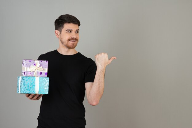 Smiling young guy holding present and show thumb up to the side.