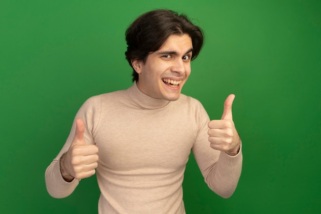 Smiling young handsome guy showing thumbs up isolated on green wall