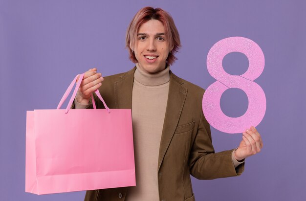 Smiling young handsome man holding pink gift bag and number eight