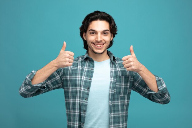 smiling young handsome man looking at camera showing thumbs up isolated on blue background