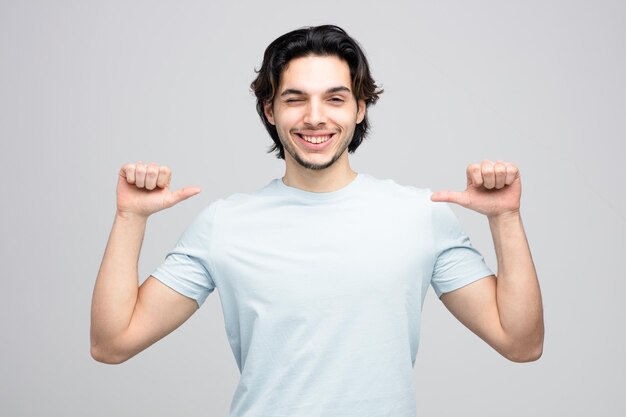 smiling young handsome man looking at camera winking pointing at himself isolated on white background