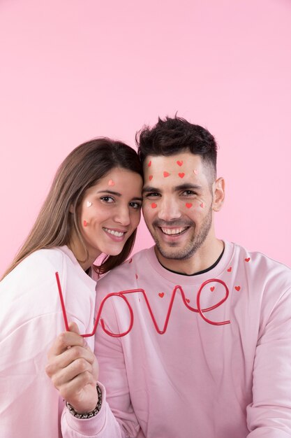 Smiling young lady and guy with paper hearts on faces and love sign