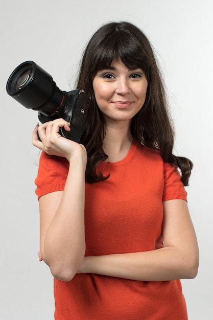 smiling young lady holding photocamera in designed t-shirt in good mood with long hair on white