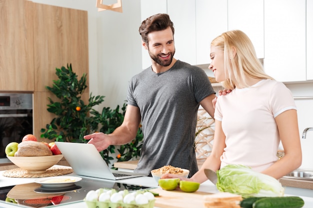 Smiling young loving couple cooking together using laptop