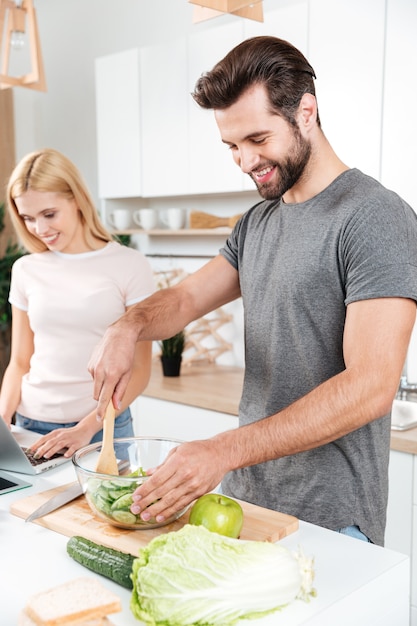 Smiling young loving couple cooking together using laptop