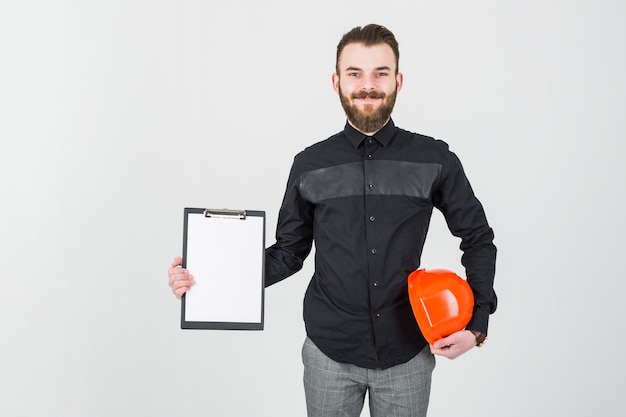 Free photo smiling young male architect holding hardhat and clipboard