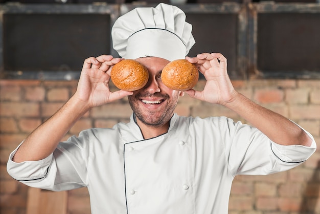 Free photo smiling young male baker holding bun over the eyes