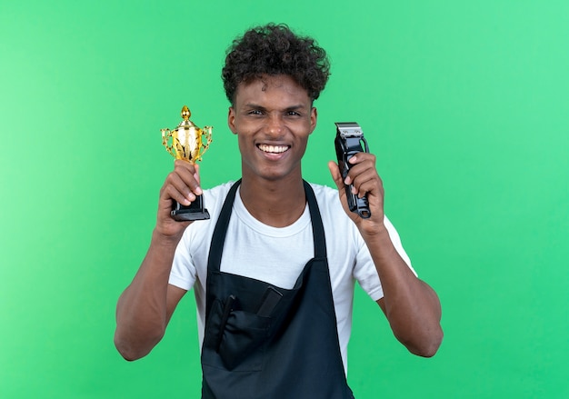 Smiling young male barber wearing uniform holding winner cup with hair