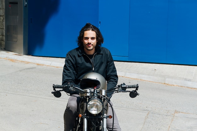 Free photo smiling young male biker sitting on motorbike looking at camera