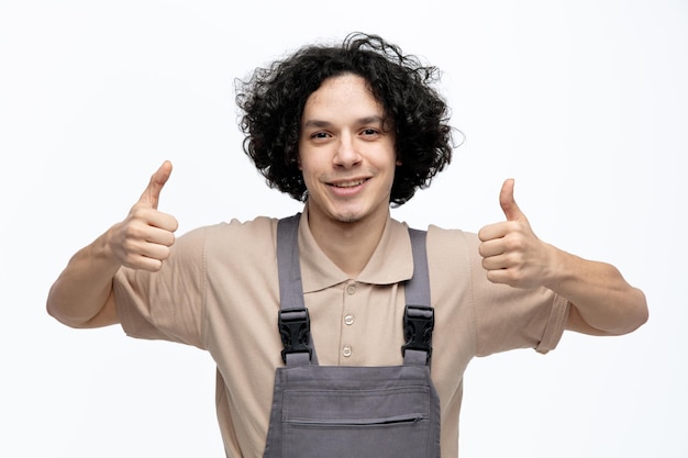 Free Photo smiling young male construction worker wearing uniform looking at camera showing thumbs up isolated on white background