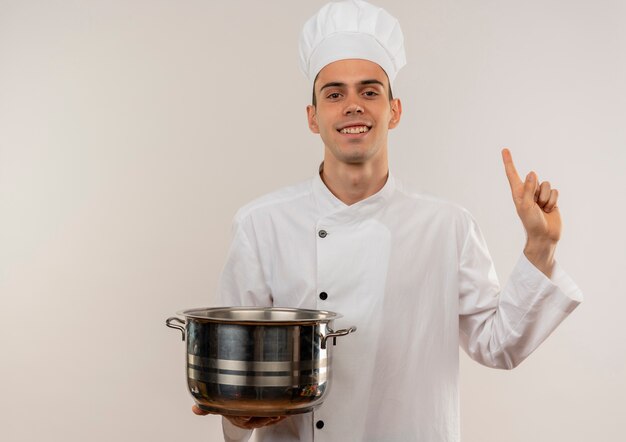 Smiling young male cook wearing chef uniform holding saucepan points finger to up with copy space