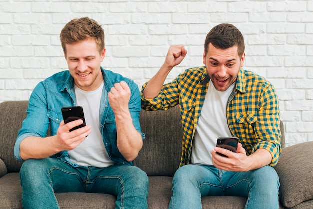 Smiling young male friends looking at smart phone clenching their fist