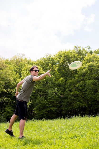 Free photo smiling young male throwing plate for frisbee on meadow