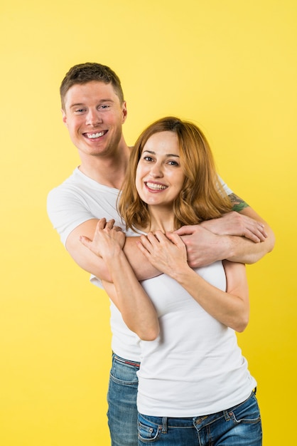 Smiling young man embracing her girlfriend against yellow backdrop