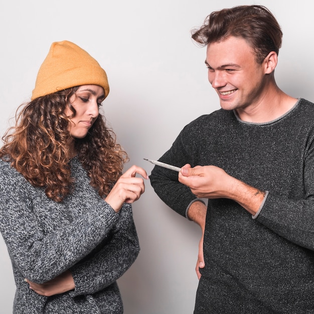 Smiling young man giving thermometer to her girlfriend