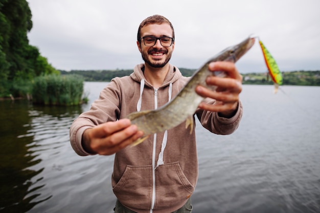 Free photo smiling young man holding fresh water fish with lure