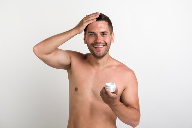 Smiling young man holding hair cream container and looking at camera