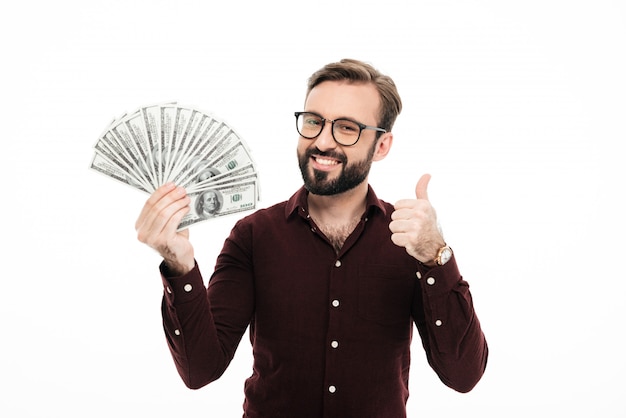 Smiling young man holding money showing thumbs up.