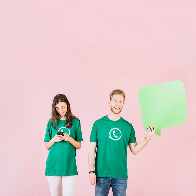 Smiling young man holding speech bubble beside woman using smartphone