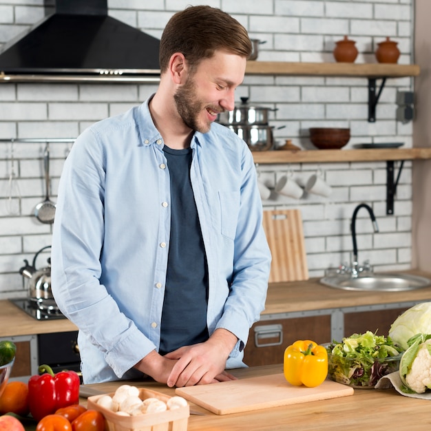 Smiling young man looking at fresh vegetables on kitchen counter