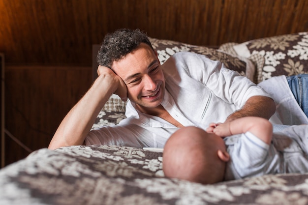 Smiling young man lying with his baby on bed