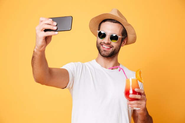 Smiling young man make selfie by phone holding cocktail.