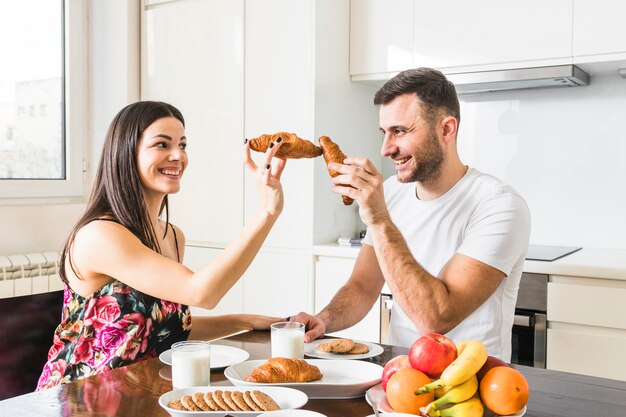 Smiling young man playing with croissant in the kitchen