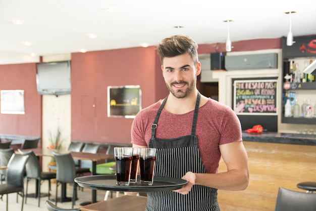 Smiling young man serving glasses of drinks in the restaurant