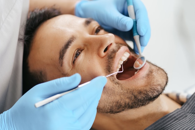 Smiling young man sitting in dentist chair while doctor examining his teeth